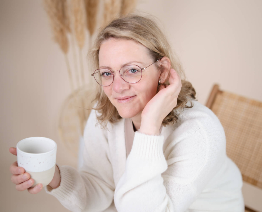 Claudia Sontheimer sitzt lächelnd mit einer Tasse Tee in der Hand und blickt freundlich in die Kamera